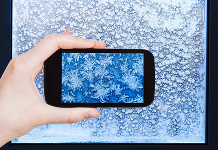 旅行概念游客用智能手机拍摄冬季寒冷夜晚窗户上的雪花和霜冻模式图片