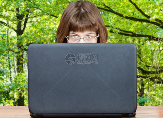 带着眼镜的女孩看露天笔记本电脑的封面绿色夏月森林在背景上图片