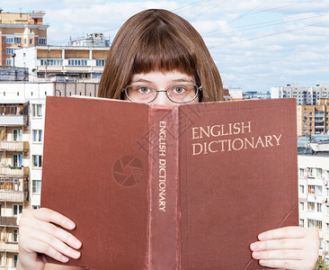 带着眼镜的女孩看着英文字典本背景是城市风背景图片
