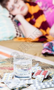 桌子上装着玻璃水和药用剂的病人背在床边的睡房里在沙发上戴围巾的有病妇女图片