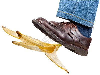 穿着牛仔裤和棕色鞋子的男左腿和棕色鞋在白背景孤立的香蕉皮上图片