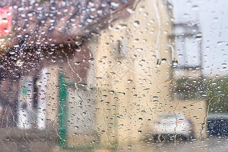 在雨中驾驶汽车风屏上的雨滴子和背景模糊房屋图片