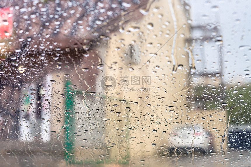 在雨中驾驶汽车风屏上的雨滴子和背景模糊房屋图片