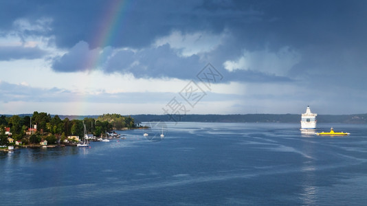 瑞典阳光明媚的秋天海滨和深蓝雨云的村庄波罗海上空有彩虹图片