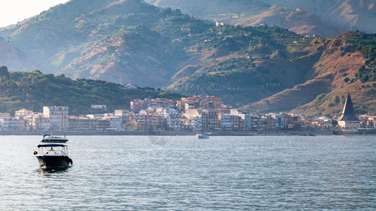 纳克索斯镇前往意大利西里夏季晚上在爱奥尼亚海的船和GiardiniNaxos镇的风景背景