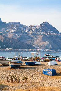前往意大利西里夏季在GiardiniNaxos镇旧港口海滩上的船只和Taormina市角斗篷的景色图片