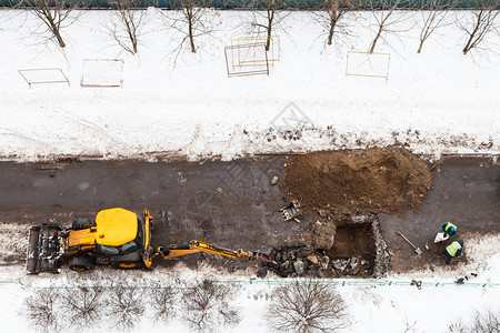 在莫斯科市冬季改变下水道管的工人和拖拉机挖掘道路图片