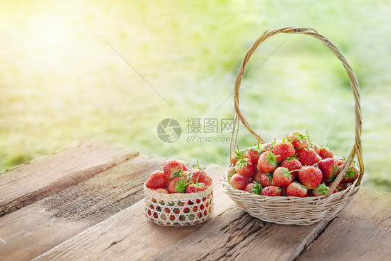 新鲜成熟的草莓在绿田背景的木地板上在篮子以绿田背景为图片