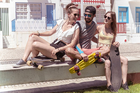 三名活跃的年轻朋友在葡萄牙阿韦罗Aveiro典型的科斯塔诺瓦住宅附近享受阳光明媚的暑假滑板图片