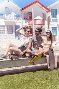 三名活跃的年轻朋友在葡萄牙阿韦罗Aveiro典型的科斯塔诺瓦住宅附近享受阳光明媚的暑假滑板图片