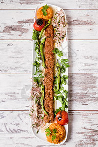 Adanakebab在白盘中配有绿色蔬菜图片