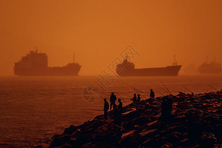 日落时停靠在岸外的货轮和鱼群渔民图片