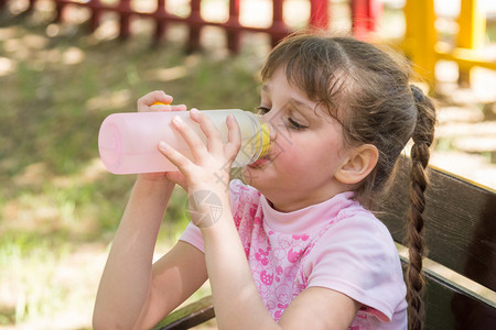 一个坐在长椅上的女孩在热天水喝瓶子里的饮用水图片