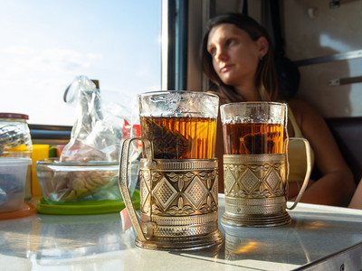 在火车厢的桌子上有杯上装着茶的金属子背景是女孩向窗外看图片