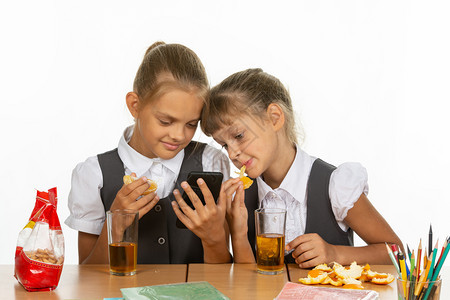 两个女学生在休息时看一智能手机的屏幕吃橙子喝果汁图片