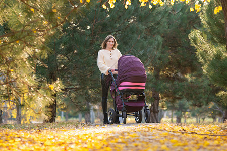 年轻母亲在秋天广场散步时骑着婴儿车的年轻母亲图片