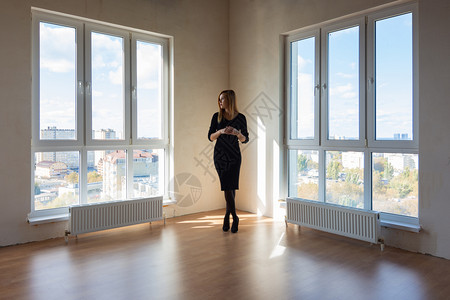 一个穿黑衣服的女孩站在两个大窗户之间在一个宽敞空旷的公寓里图片