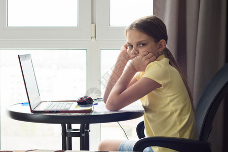 一个不高兴的女孩坐在家里桌子上做功课看着不高兴图片
