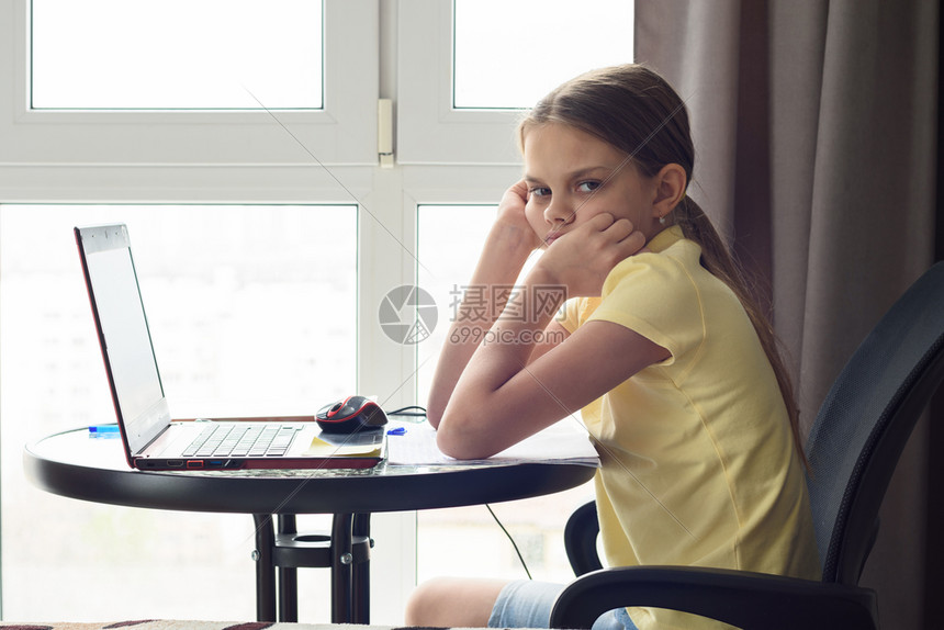一个不高兴的女孩坐在家里桌子上做功课看着不高兴图片