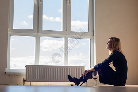 坐在窗边的可悲女孩坐在一个空公寓里喝着一杯葡萄酒图片