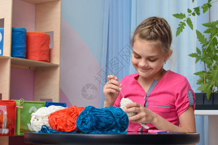 女孩在儿童房间室内的一张桌子上坐在一个儿童房间的张桌子上织着一个柔软的玩具图片