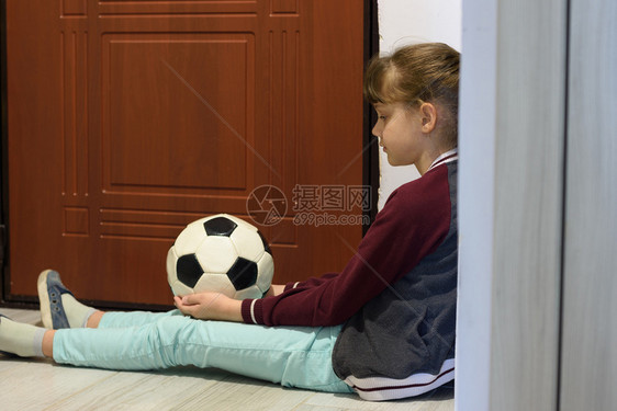 被隔离的孤独女孩坐在门前与一个球坐在前门图片