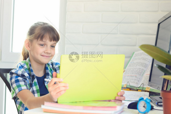 女孩坐在桌子上愉快地看着平板电脑的屏幕图片