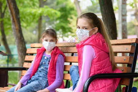 身戴医疗保护面罩的女童坐在操场长凳上图片