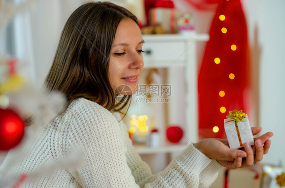 美丽的年轻女孩看着可爱的礼物在装饰圣诞礼堂图片