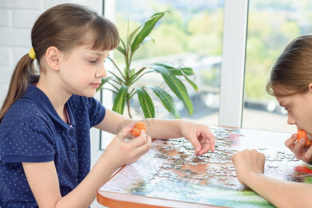 两个女孩在桌边收集拼图吃胡萝卜背景图片