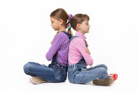 两个争吵的女孩坐在彼此背对的白色景上图片