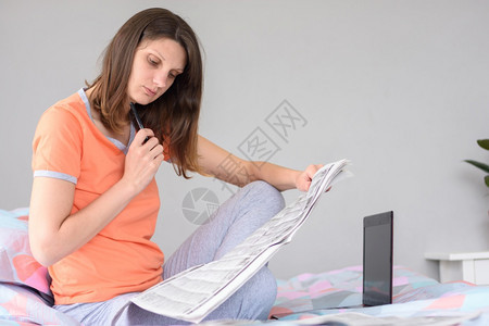 一个女孩正在寻找工作通过报纸广告寻找工作在笔记本电脑旁边图片
