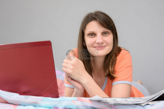女孩躺在床上带着笔记本电脑和报纸躺在床上并喜悦地看着框架图片