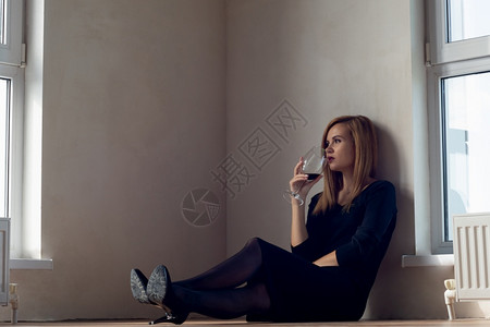 女孩坐在大窗户附近的地板上喝酒图片