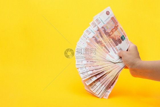 手握着一包五千张俄罗斯钞票的粉丝在黄色背景上图片