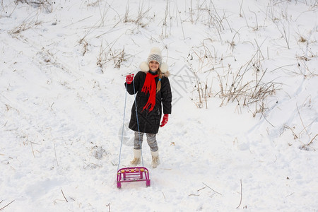一个女孩带着雪橇站在地草上图片