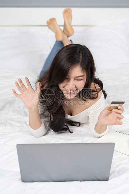 高兴的妇女在网上购物床用信卡和笔记本电脑购买信用卡和笔记本电脑图片