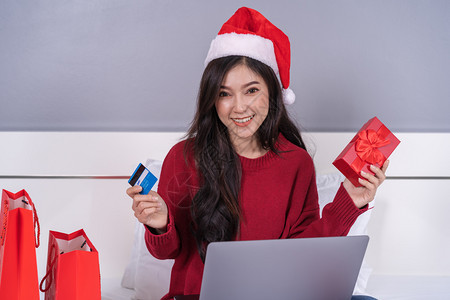 网上买圣诞礼物的幸福妇女床上有电脑笔记本和信用卡图片