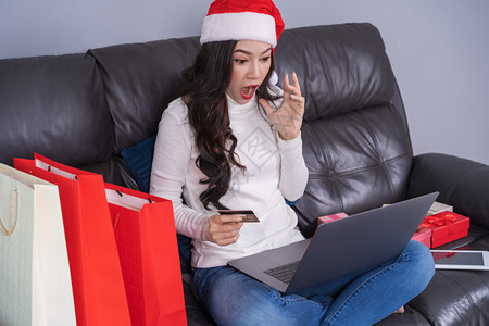 令人惊讶的女在圣塔帽购物线买圣诞礼物在客厅用笔记本电脑图片