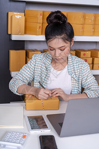 小型在线企业拥有者从事膝上型计算机工作的妇女准备包裹箱以便交给客户图片