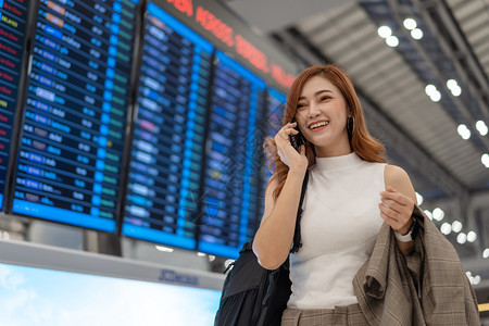 在机场飞行信息板上接听移动电话的美丽女旅行者图片