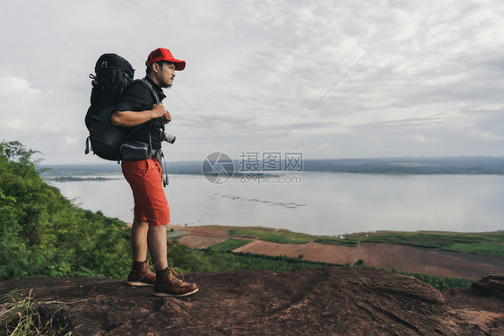 在悬崖边缘岩山顶上背着包的男旅行者图片