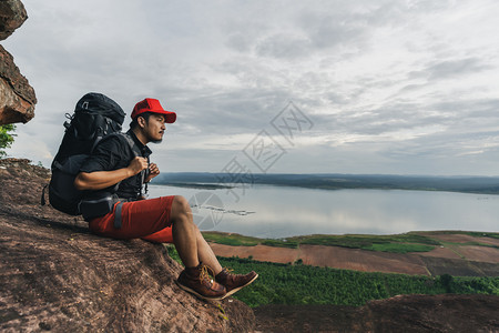 男人旅行者背着包坐在悬崖边缘岩石山顶图片