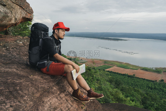 男人旅行者背着包坐在悬崖边缘岩石山顶图片