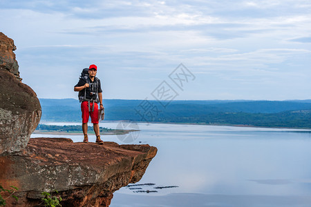 在悬崖边缘岩山顶上背着包的男旅行者图片