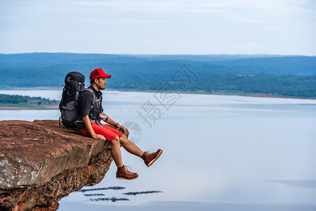 男人旅行者背着包坐在悬崖边缘岩石山顶图片