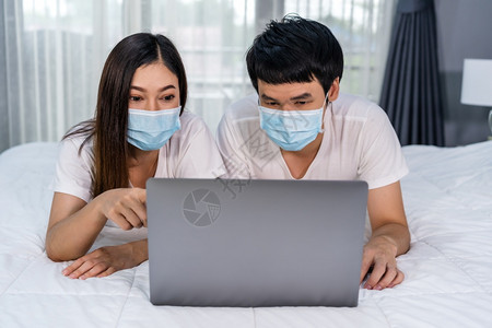 在检疫大流行冠状新冠住院期间夫妇用膝上型电脑在床戴医疗面罩图片