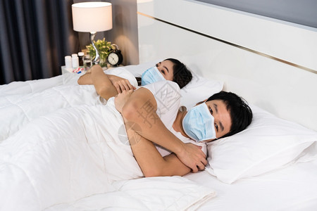 有病的夫妇在床上感到寒冷并戴医疗面具以保护冠状新冠大流行病图片