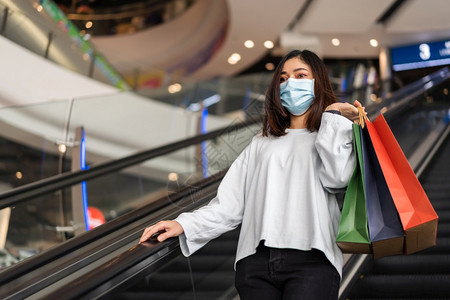 年轻妇女在商场用包购物并戴医疗面具以防止科罗纳新冠大流行图片