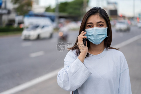 年轻妇女在城市街道上与移动电话交谈并戴面罩保护传播冠状新冠流行病这是新的正常概念图片